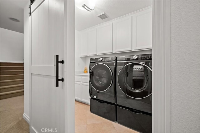 laundry room featuring a barn door, light tile patterned flooring, separate washer and dryer, visible vents, and cabinet space