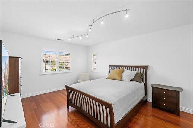 bedroom featuring dark wood-style floors, track lighting, visible vents, and baseboards