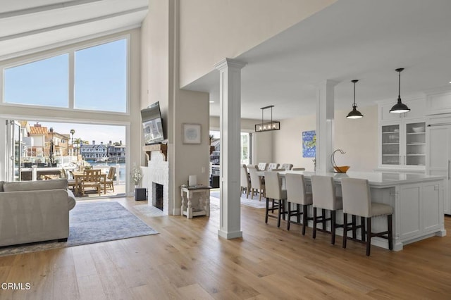 interior space with a high ceiling, a fireplace with flush hearth, baseboards, light wood-type flooring, and decorative columns