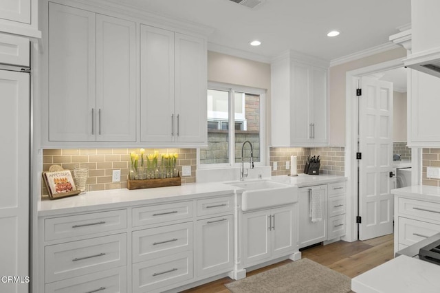 kitchen featuring a sink, light wood-style floors, white cabinets, light countertops, and crown molding