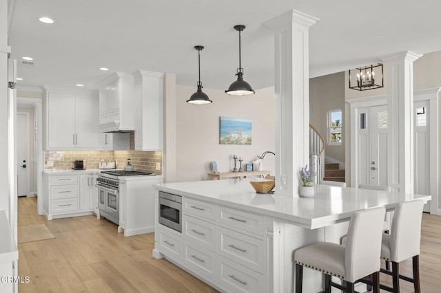 kitchen featuring decorative columns, light wood finished floors, stainless steel appliances, light countertops, and white cabinets