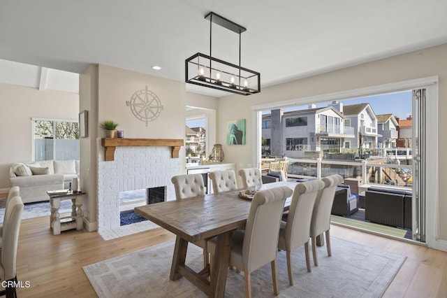 dining room with light wood-type flooring, a brick fireplace, plenty of natural light, and baseboards