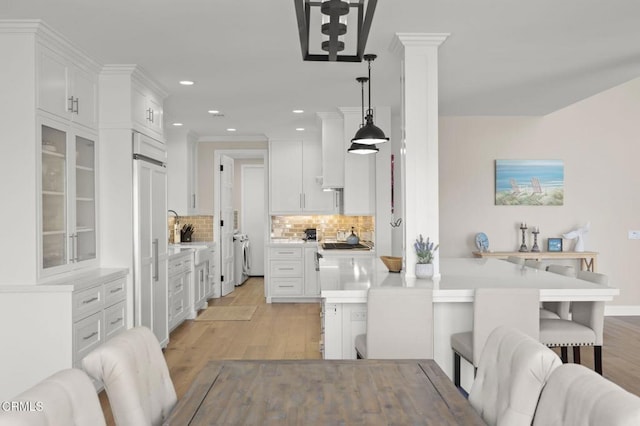 kitchen featuring pendant lighting, a breakfast bar area, tasteful backsplash, light countertops, and white cabinetry