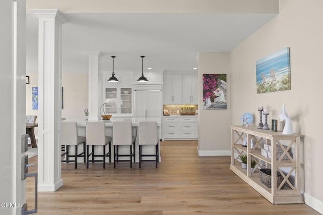 kitchen with a breakfast bar, white cabinets, light countertops, decorative light fixtures, and ornate columns