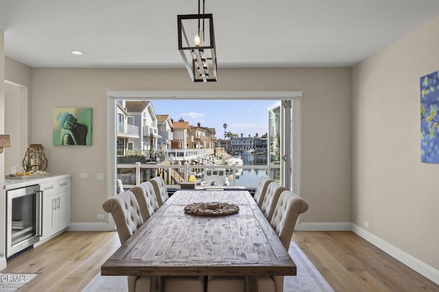 dining area with light wood finished floors, wine cooler, a water view, and baseboards