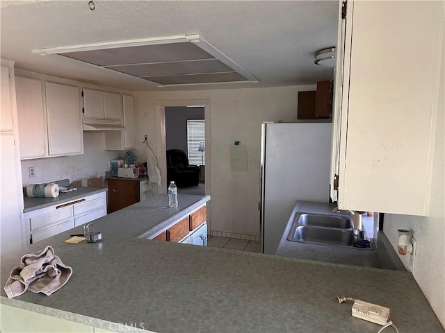 kitchen featuring freestanding refrigerator, white cabinetry, a sink, and a peninsula