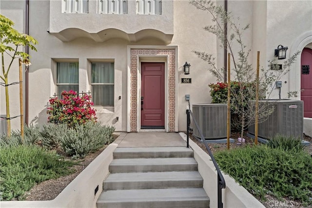 property entrance with stone siding, central AC unit, and stucco siding