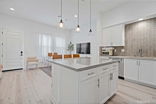 kitchen featuring light countertops, hanging light fixtures, white cabinetry, a sink, and dishwasher