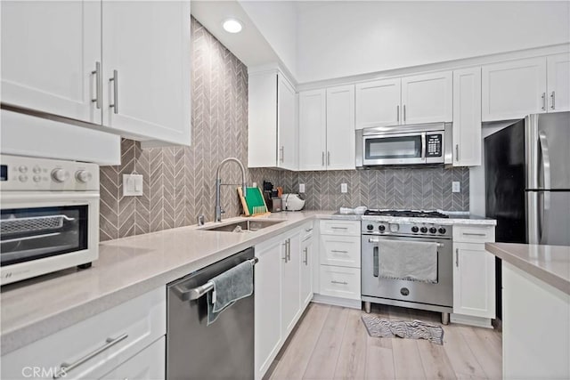 kitchen with light wood-style flooring, stainless steel appliances, a sink, white cabinets, and decorative backsplash