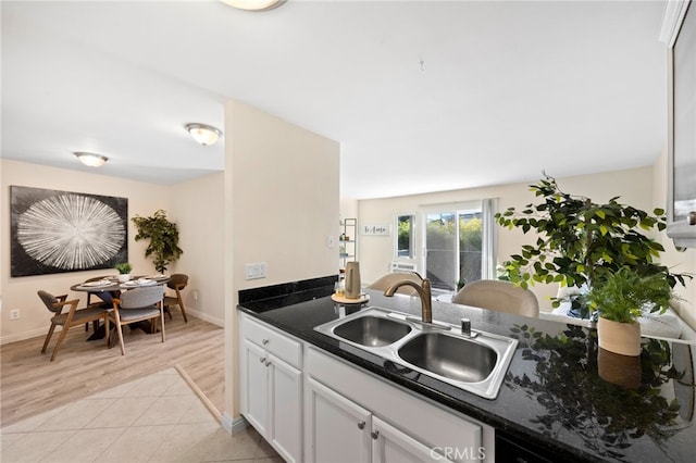 kitchen with light tile patterned flooring, a sink, white cabinetry, baseboards, and dark stone counters