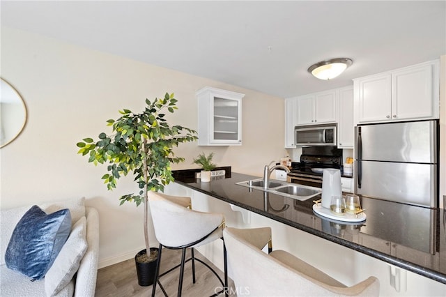 kitchen featuring stainless steel appliances, glass insert cabinets, white cabinetry, dark stone countertops, and a kitchen breakfast bar