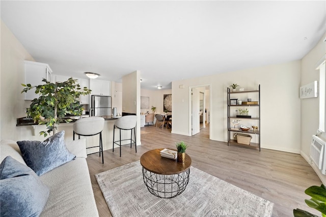 living room featuring light wood-style floors, baseboards, and an AC wall unit