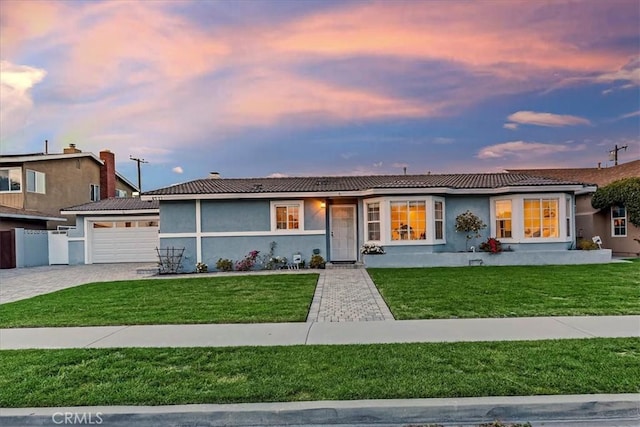 ranch-style house featuring a yard, decorative driveway, an attached garage, and stucco siding