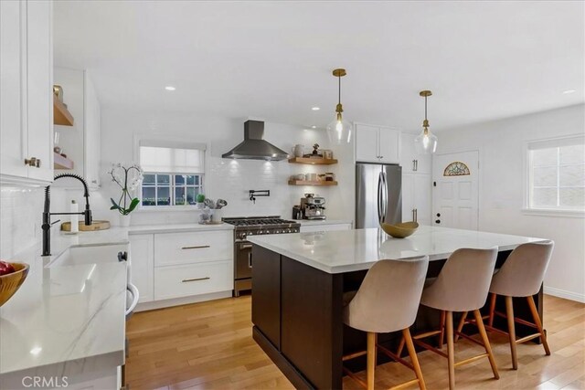 kitchen featuring open shelves, white cabinetry, appliances with stainless steel finishes, light wood-type flooring, and wall chimney exhaust hood