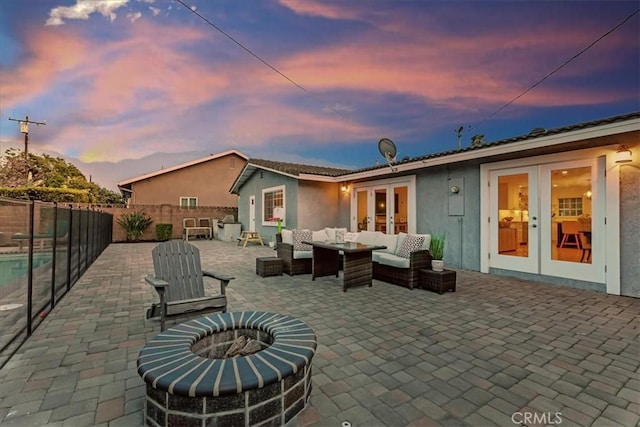 rear view of house with an outdoor living space with a fire pit, fence, french doors, a patio area, and stucco siding