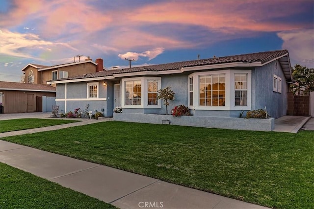 ranch-style house featuring a tile roof, a yard, fence, and stucco siding