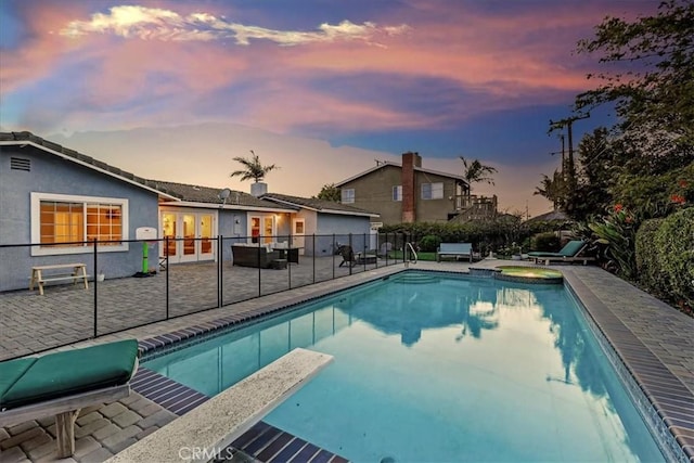 pool at dusk with a patio area, fence, a diving board, and a fenced in pool