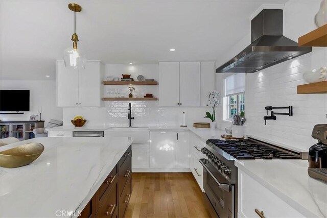 kitchen with light stone counters, stainless steel stove, a sink, wall chimney range hood, and open shelves