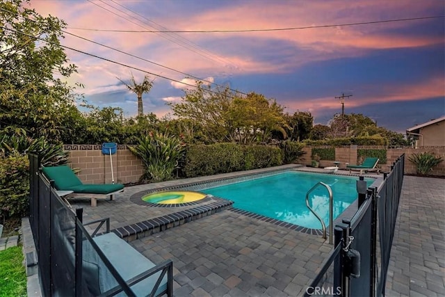 pool at dusk with a patio, a fenced backyard, a fenced in pool, and an in ground hot tub