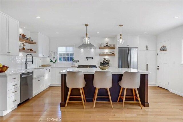 kitchen featuring a center island, stainless steel appliances, light countertops, open shelves, and a sink