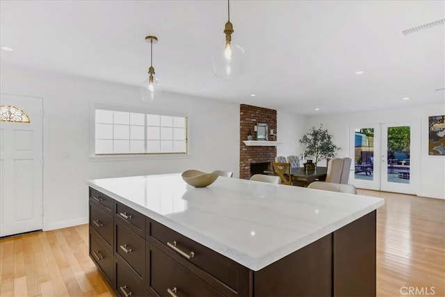 kitchen with visible vents, light countertops, a brick fireplace, light wood finished floors, and decorative light fixtures