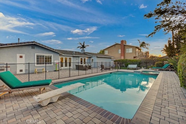 view of swimming pool featuring fence, french doors, a patio area, a pool with connected hot tub, and a diving board