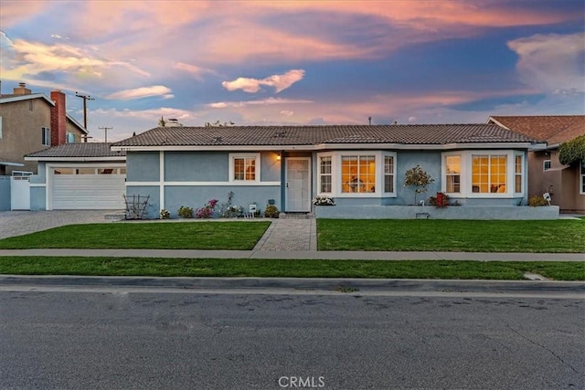 ranch-style home with an attached garage, decorative driveway, a lawn, and stucco siding