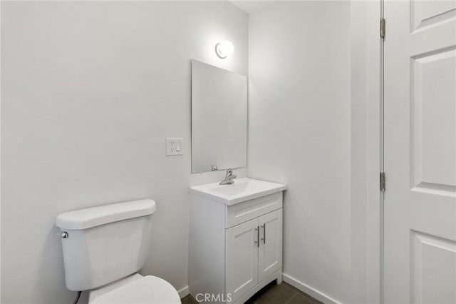 half bath with toilet, tile patterned floors, vanity, and baseboards