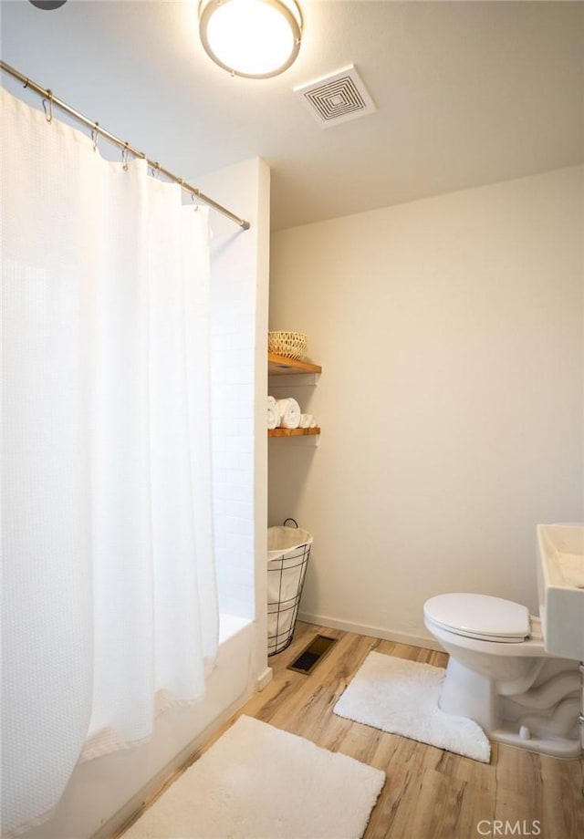 bathroom with toilet, visible vents, wood finished floors, and shower / tub combo with curtain