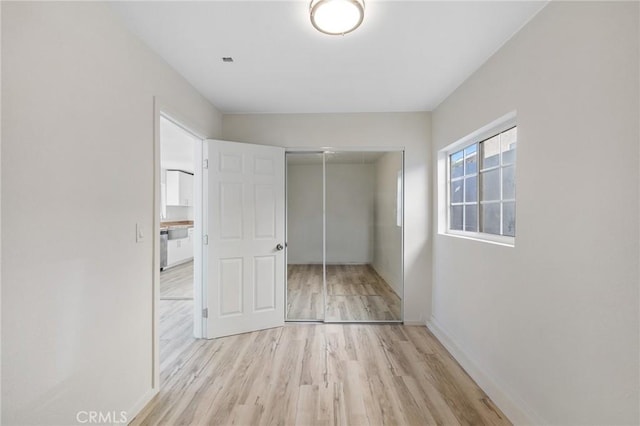 unfurnished bedroom with light wood-type flooring, baseboards, and a closet