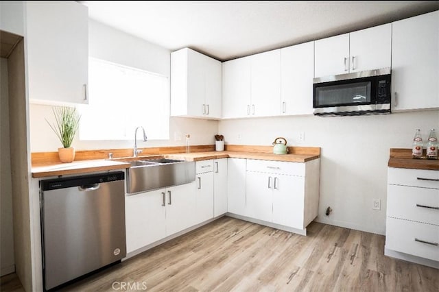 kitchen with stainless steel appliances, light wood-type flooring, a sink, and white cabinetry