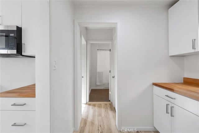 kitchen with light wood finished floors, white cabinetry, stainless steel microwave, and baseboards