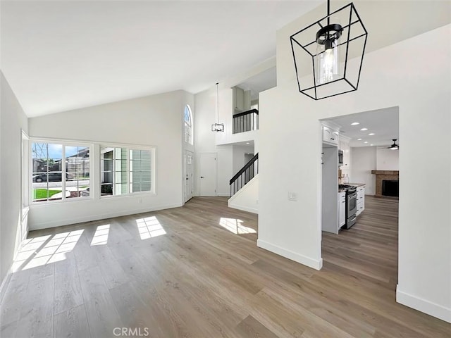 unfurnished living room with high vaulted ceiling, a fireplace, baseboards, light wood-style floors, and stairway