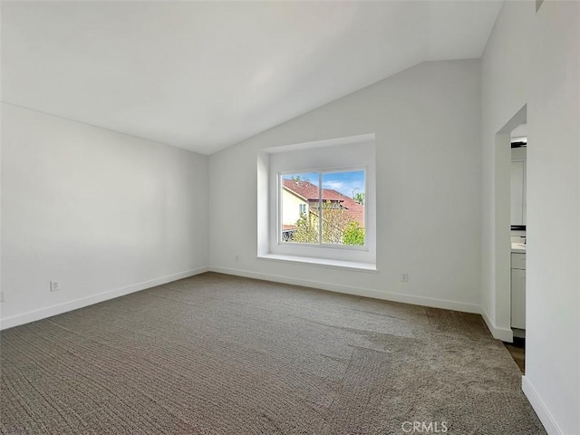 spare room featuring vaulted ceiling, dark colored carpet, and baseboards