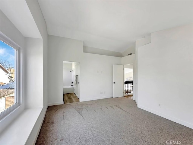 unfurnished bedroom featuring lofted ceiling, multiple windows, baseboards, and light colored carpet