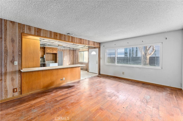 kitchen with visible vents, a peninsula, light wood-style flooring, and wooden walls