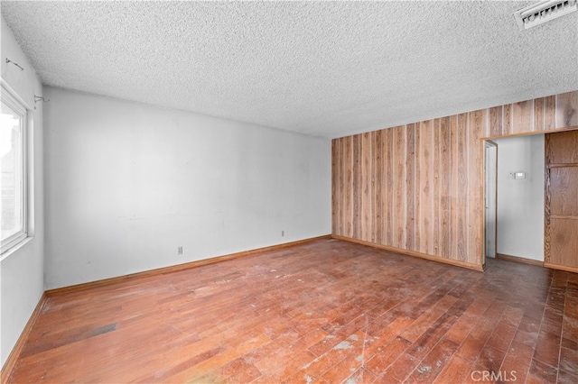 spare room featuring a textured ceiling, hardwood / wood-style floors, visible vents, and wooden walls