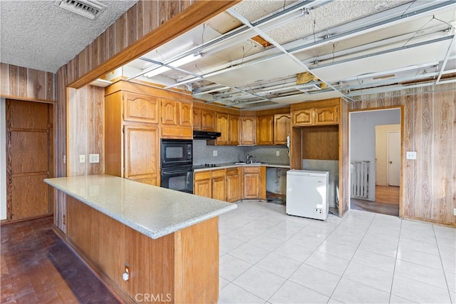 kitchen with light countertops, visible vents, a peninsula, under cabinet range hood, and black appliances