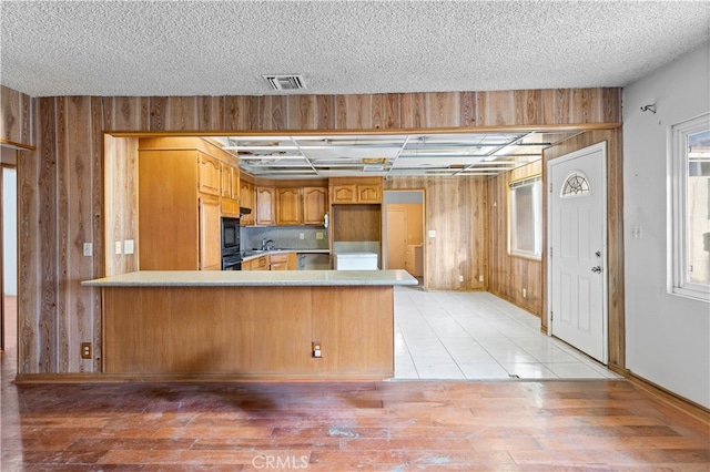 kitchen with visible vents, a peninsula, light countertops, wood walls, and a sink