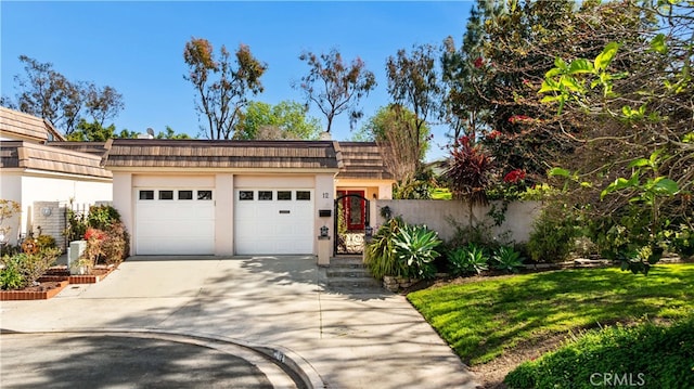 view of front of house with driveway, mansard roof, an attached garage, fence, and stucco siding