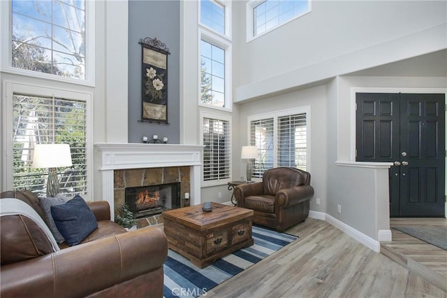 living area with a towering ceiling, light wood-style flooring, baseboards, and a tile fireplace