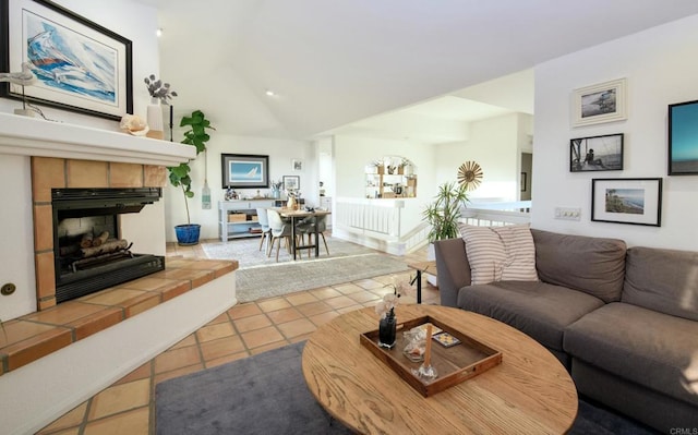 living room featuring a tile fireplace, vaulted ceiling, and light tile patterned floors