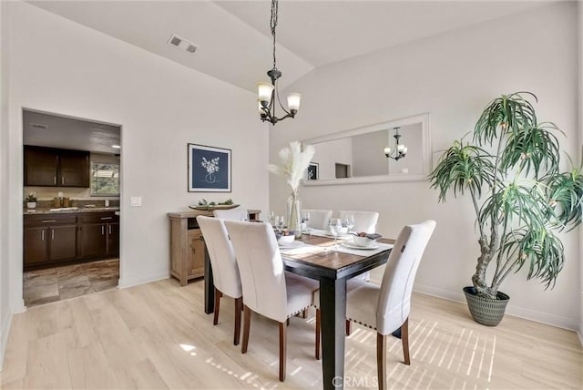 dining space featuring vaulted ceiling, light wood finished floors, visible vents, and an inviting chandelier