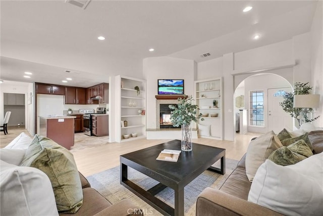 living area featuring arched walkways, recessed lighting, visible vents, light wood-type flooring, and a multi sided fireplace