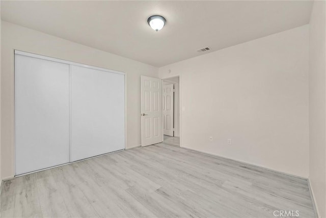 unfurnished bedroom featuring light wood finished floors, a closet, and visible vents