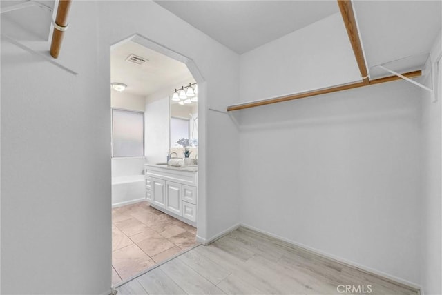 walk in closet with arched walkways, visible vents, a sink, and light wood-style flooring