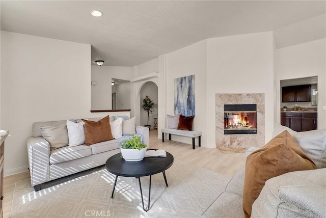 living room featuring arched walkways, recessed lighting, light wood-style flooring, and a premium fireplace