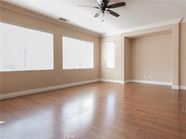 empty room with ornamental molding, wood finished floors, visible vents, and baseboards