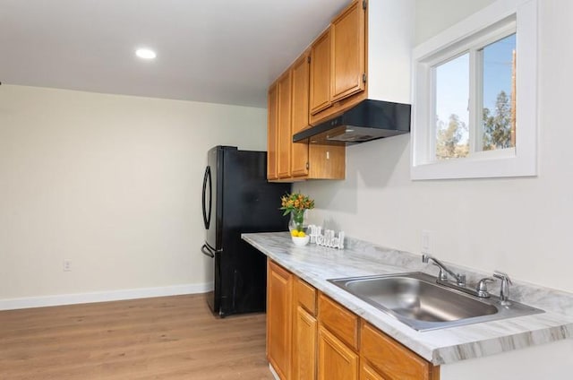 kitchen featuring freestanding refrigerator, light countertops, a sink, and under cabinet range hood