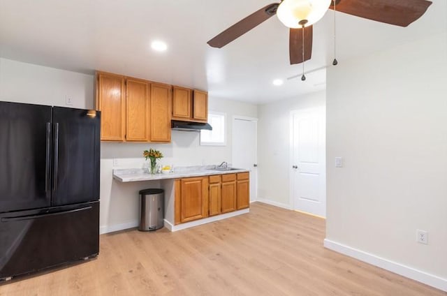 kitchen featuring light wood-style flooring, freestanding refrigerator, light countertops, and under cabinet range hood